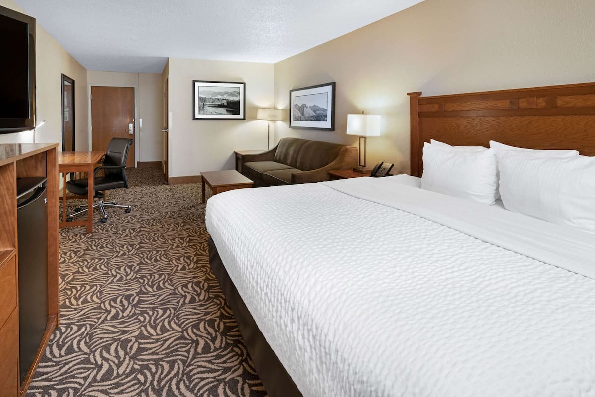 A hotel room with a large bed, a desk with a chair, a television, and framed pictures on the wall.