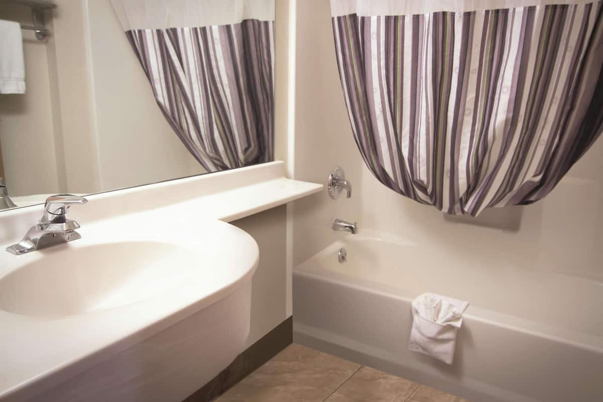 A bathroom with a white sink, a bathtub, and striped curtains.
