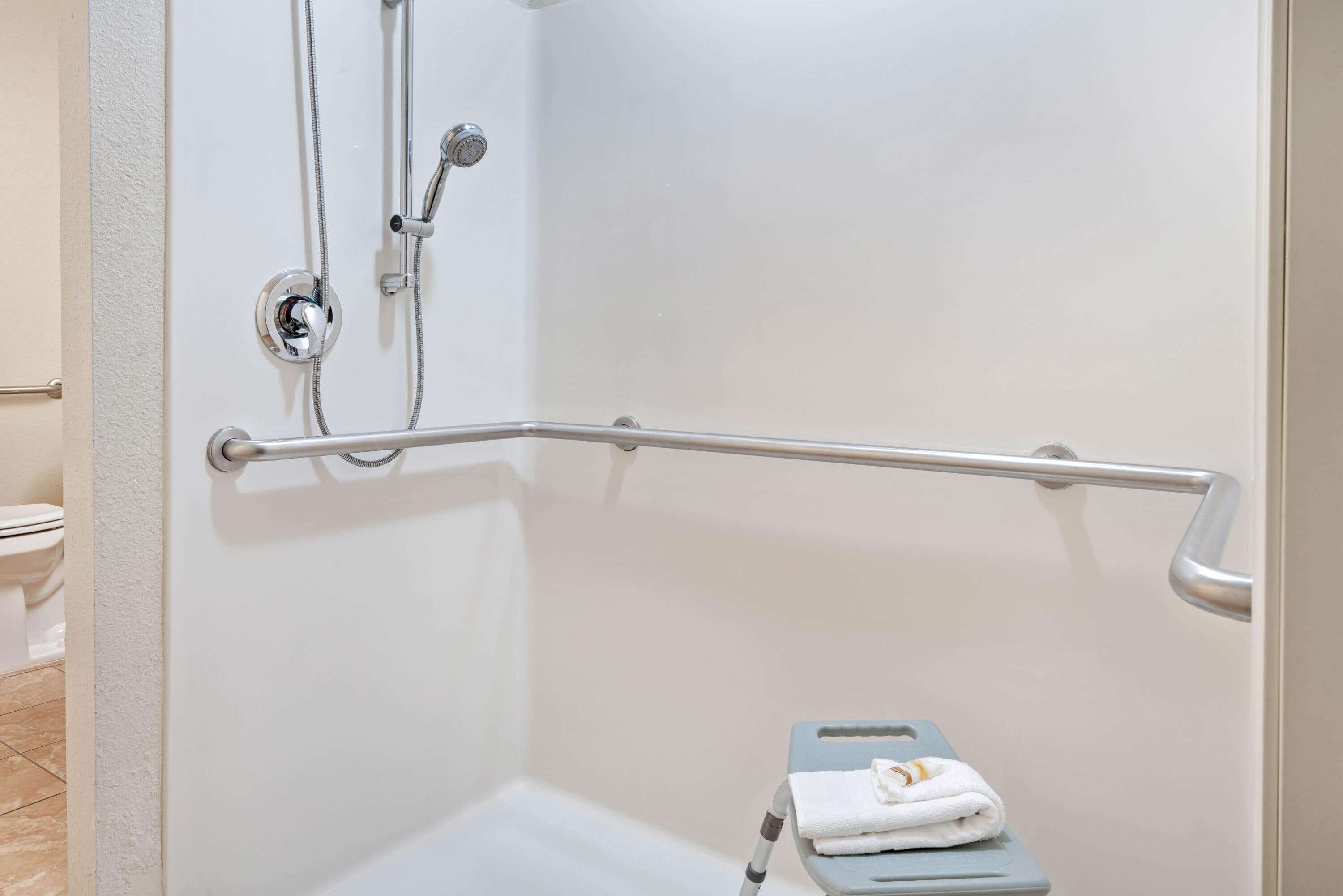 A bathroom with a shower, a grab bar, and a step stool with a towel.