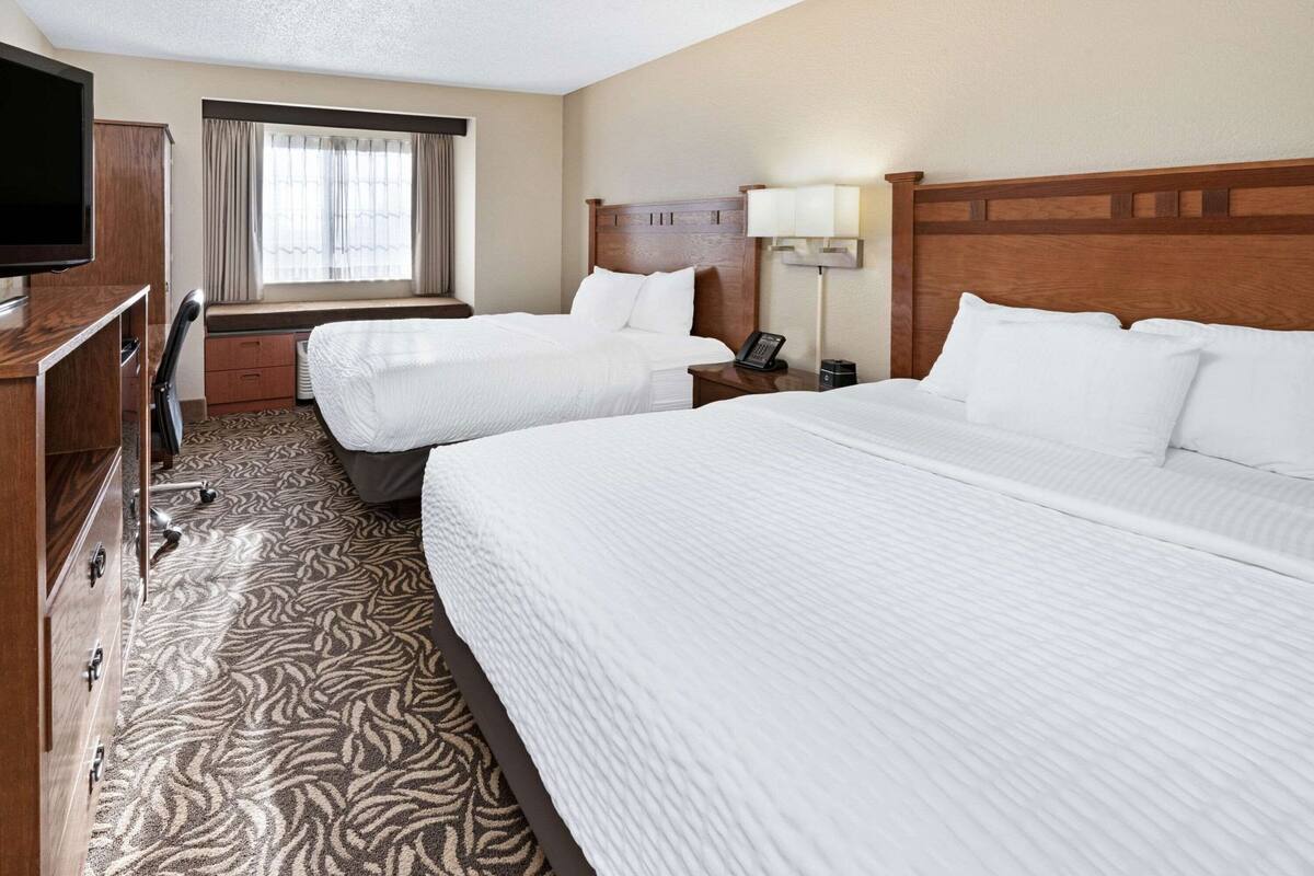 Quarto de hotel com duas camas, televisão, escrivaninha e janela com cortinas.