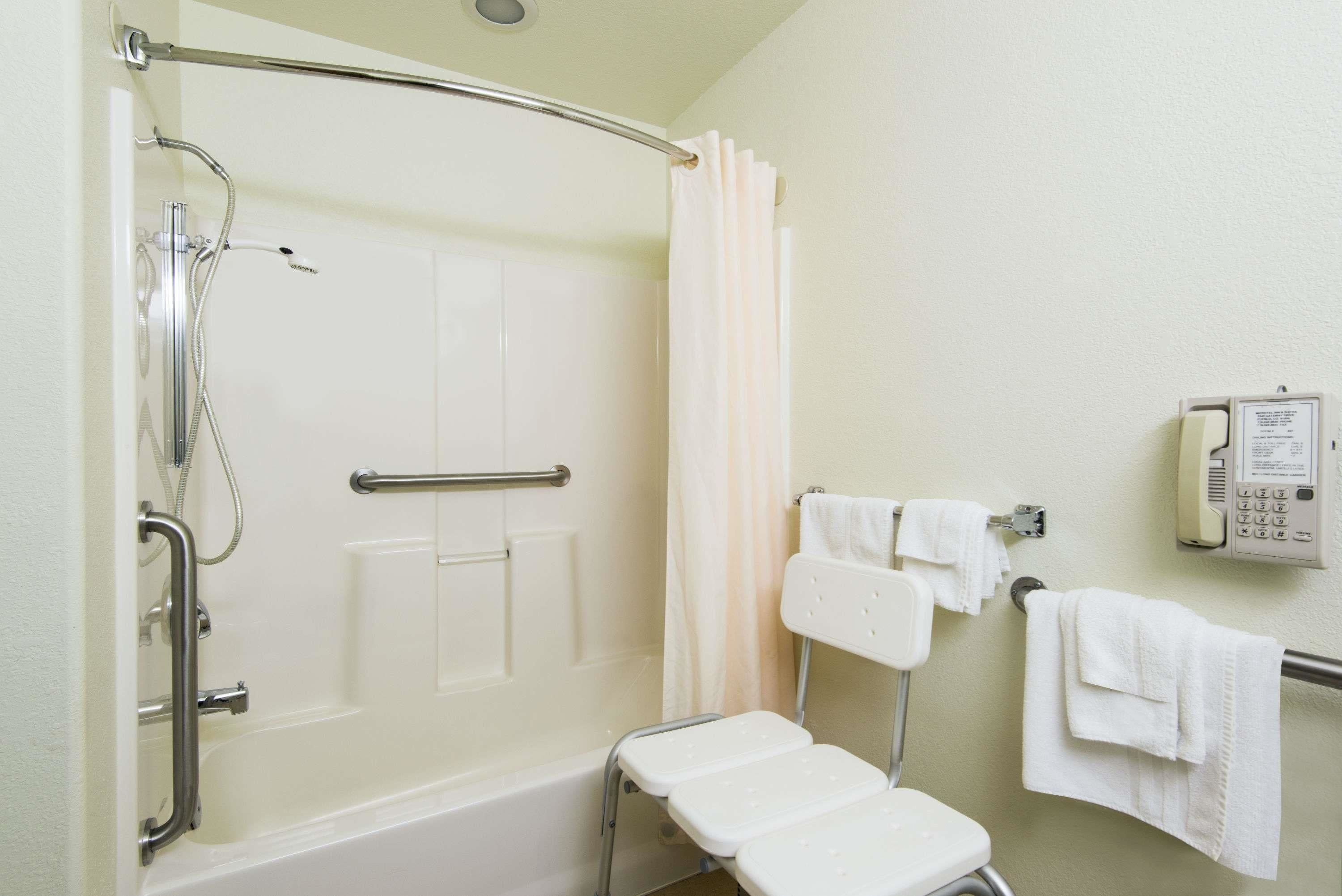 Ein Badezimmer mit Dusche, Haltegriffen, einer weißen Badewanne, einer weißen Toilette und einem Handtuchhalter mit Handtüchern.