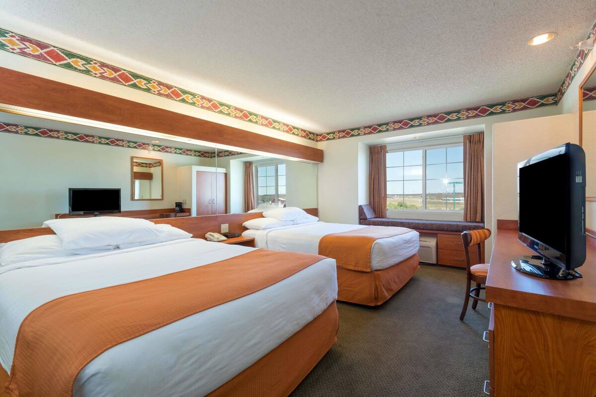 Habitación de hotel con dos camas, un escritorio con televisor, un espejo y una ventana con cortinas.