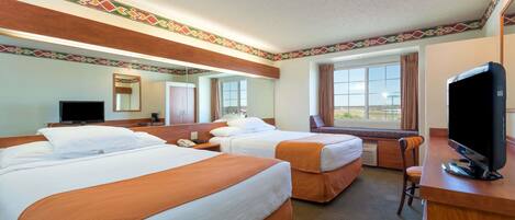 A hotel room with two beds, a desk with a television, a mirror, and a window with curtains.