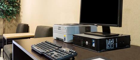 A desk with a computer setup including a monitor, keyboard, and mouse, a printer, and a plant.