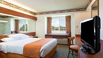 Habitación de hotel con una cama grande, televisión, escritorio y ventana con cortinas.