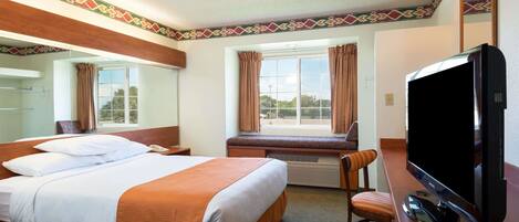 Habitación de hotel con una cama grande, televisión, escritorio y ventana con cortinas.
