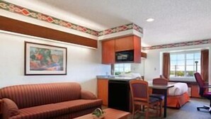 A hotel room with a sofa, a small table, a desk with a chair, a television, and a window with curtains. - Microtel Inn & Suites by Wyndham Pueblo (Pueblo)
