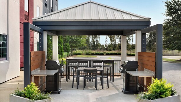 Een terras buiten met een overdekte zithoek, twee barbecues en een eettafel met stoelen.