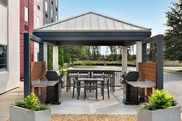 Un patio exterior con una zona de estar cubierta, dos parrillas de barbacoa y una mesa de comedor con sillas.