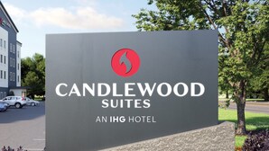 Naamplaatje voor Candlewood Suites, een IHG hotel, met een rood logo, omringd door een aangelegde tuin met diverse kleurrijke bloemen.