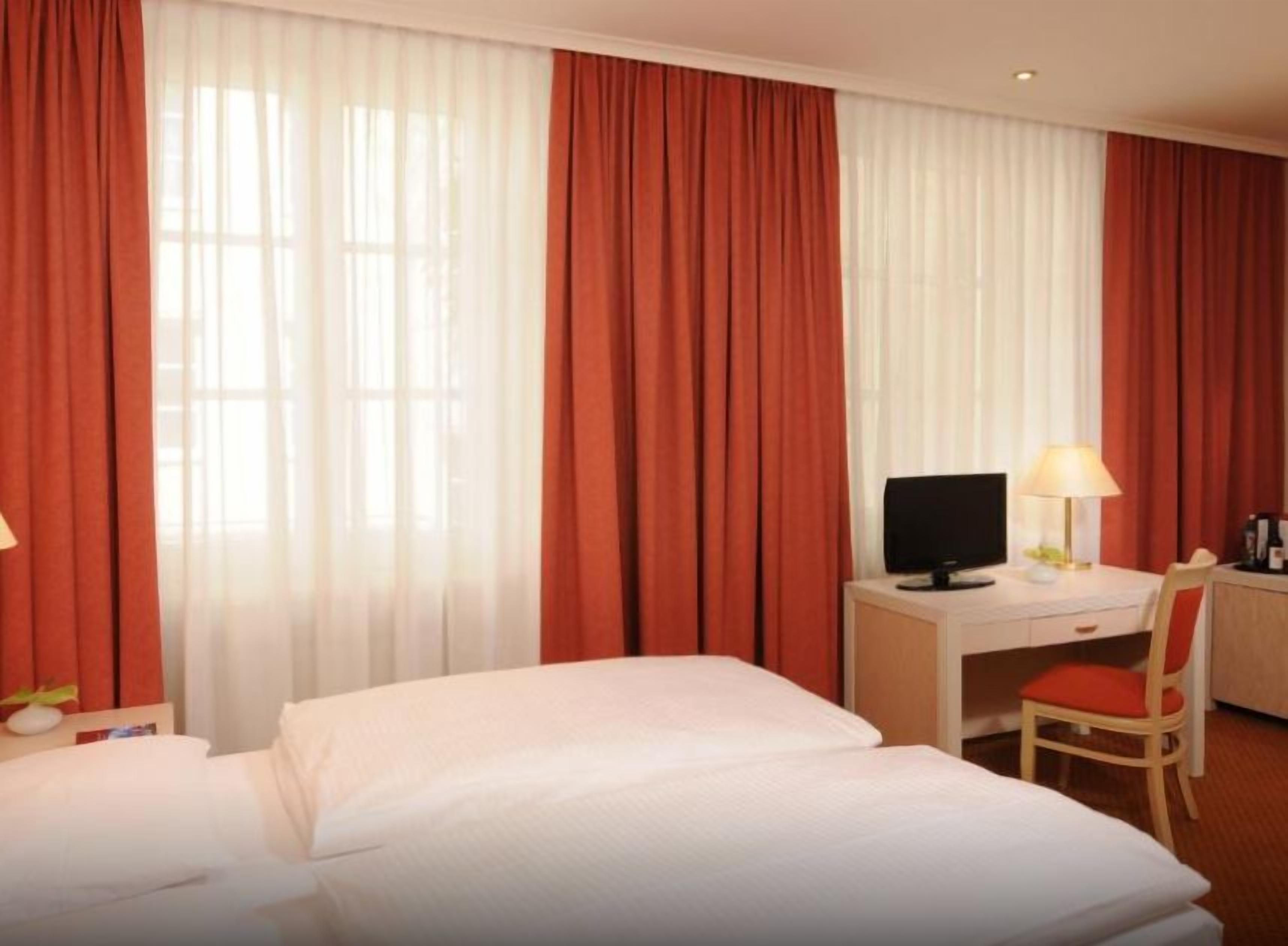 Ein Hotelzimmer mit einem Bett, einem Schreibtisch mit Computer, einem Sessel und einer Lampe.