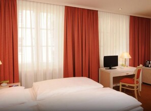 Una habitación de hotel con una cama, un escritorio con una computadora, una silla y una lámpara.