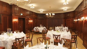 Una sala da banchetti con tavoli rotondi apparecchiati per la cena, pannelli in legno, lampadari e applique.