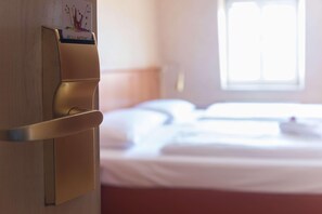 Et hotelværelse med en seng, et natbord og en oplader på væggen.
