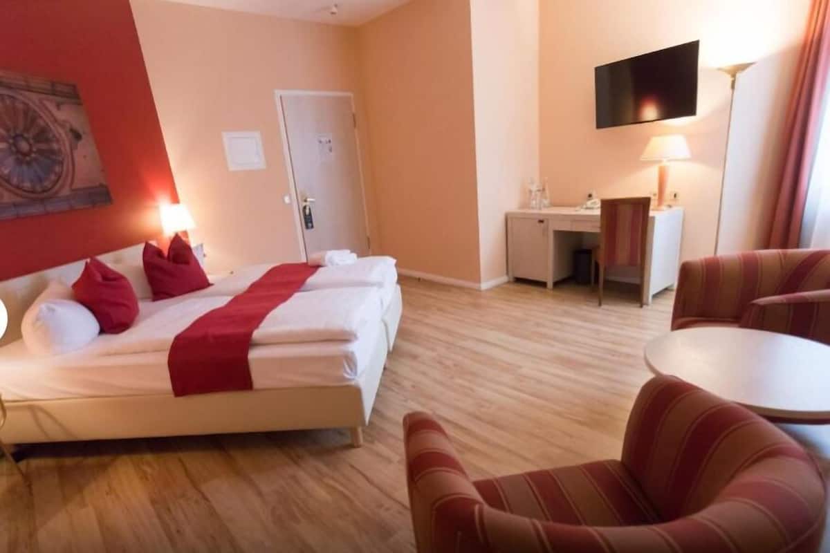 A hotel room with a bed, a desk, a chair, and a TV.
