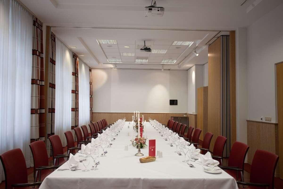 A conference room with a long table set for a meeting, red chairs, and a projector on the ceiling.