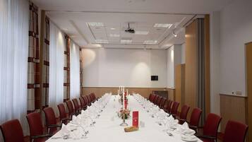 A conference room with a long table set for a meeting, red chairs, and a projector on the ceiling.