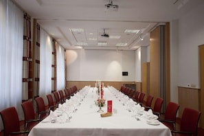A conference room with a long table set for a meeting, red chairs, and a projector on the ceiling.