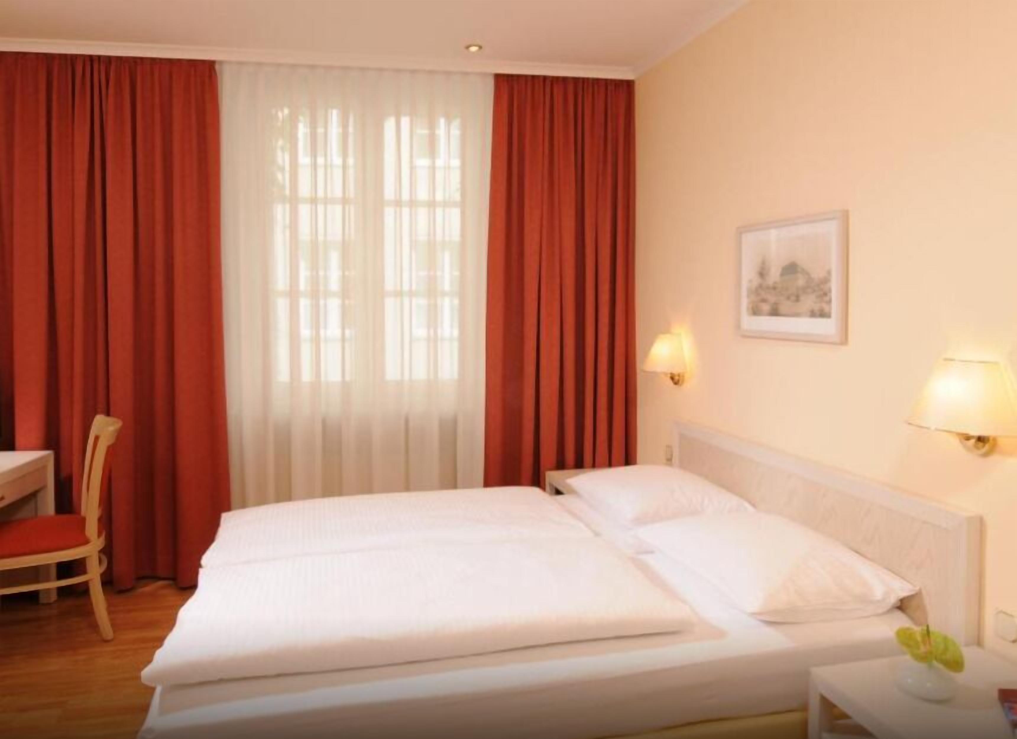A hotel room with two beds, a chair, a desk, and a lamp.