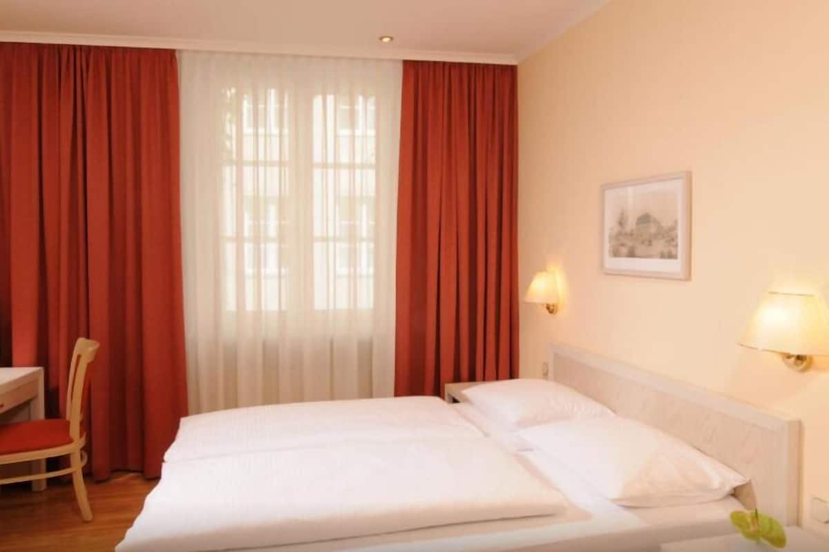 A hotel room with two beds, a chair, a desk, and a lamp.