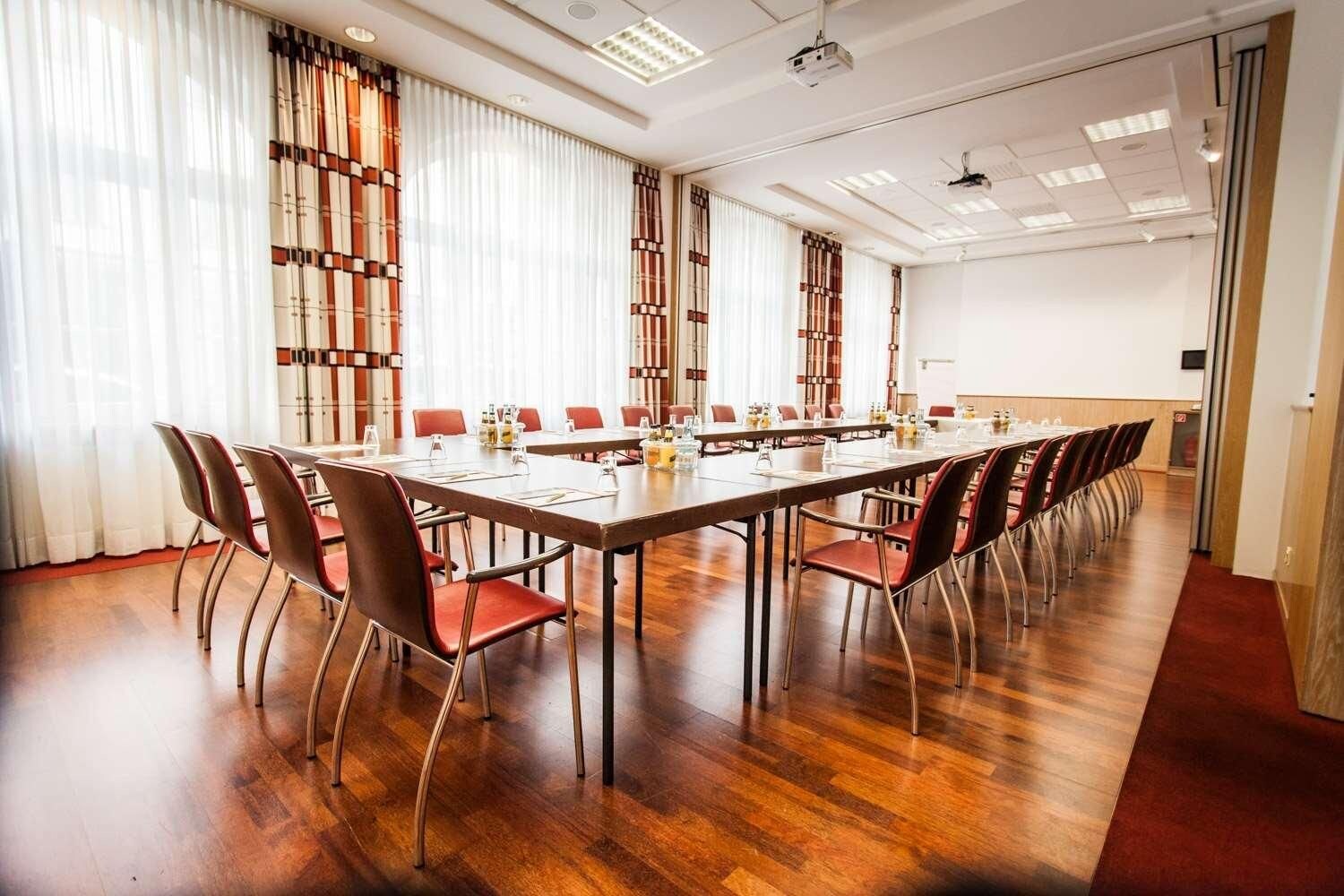 A conference room with a long table, red chairs, and a wooden floor.