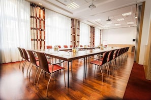 A conference room with a long table, red chairs, and a wooden floor.