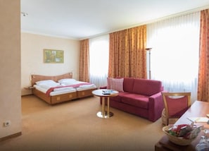 Quarto de hotel com uma cama, um sofá, uma mesinha redonda e uma janela com cortinas.