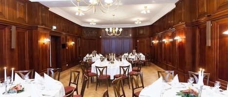 A banquet hall with round tables set for dining, wooden paneling on the walls, and chandeliers.