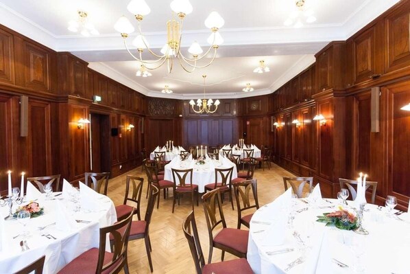A banquet hall with round tables set for dining, wooden paneling on the walls, and chandeliers.