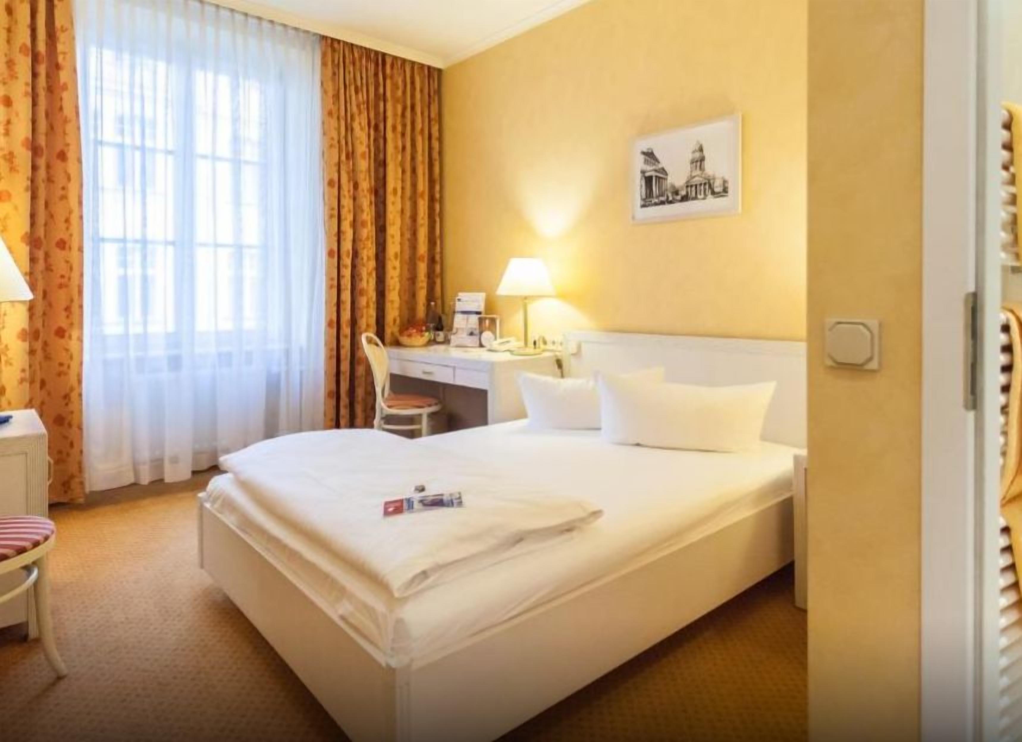 A hotel room with a bed, a desk, a chair, and a window with curtains.