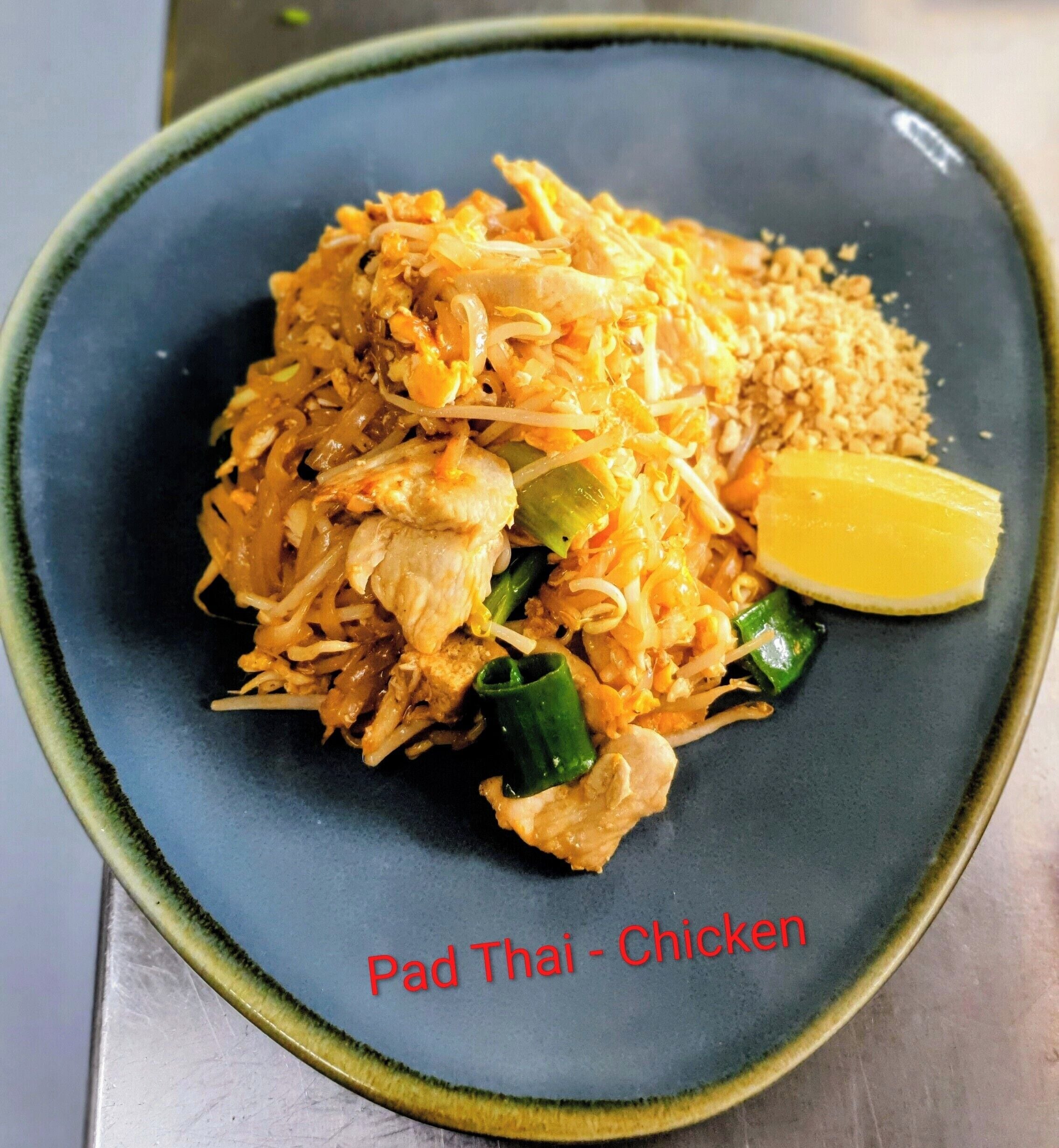 A plate of Pad Thai with chicken, served on a dark blue plate with a green rim.