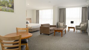 A hotel room with a bed, two sofas, a coffee table, a dining table with chairs, and a large window with curtains. - Posthouse MotorLodge (Goulburn)