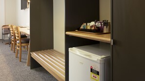 A compact kitchenette with a white refrigerator, a wooden bench, and a shelf with kitchen essentials. - Posthouse MotorLodge (Goulburn)