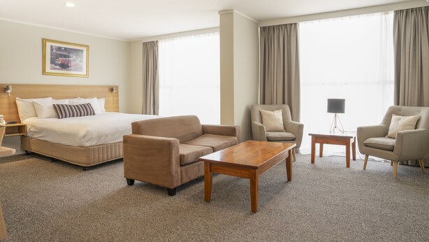 A hotel room with a bed, two armchairs, a sofa, a coffee table, and a TV. - Posthouse MotorLodge (Goulburn)