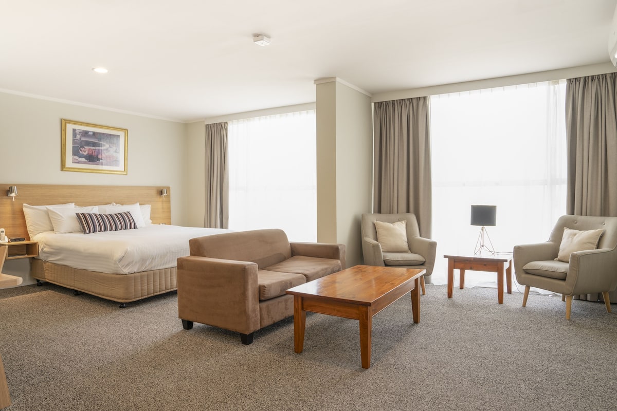 A hotel room with a bed, two armchairs, a sofa, a coffee table, and a TV.