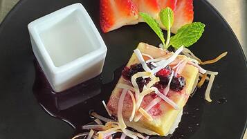 Un dessert à base de riz gluant, de crème pâtissière thaïlandaise, de fraises et de feuilles de menthe, présenté sur une assiette noire.