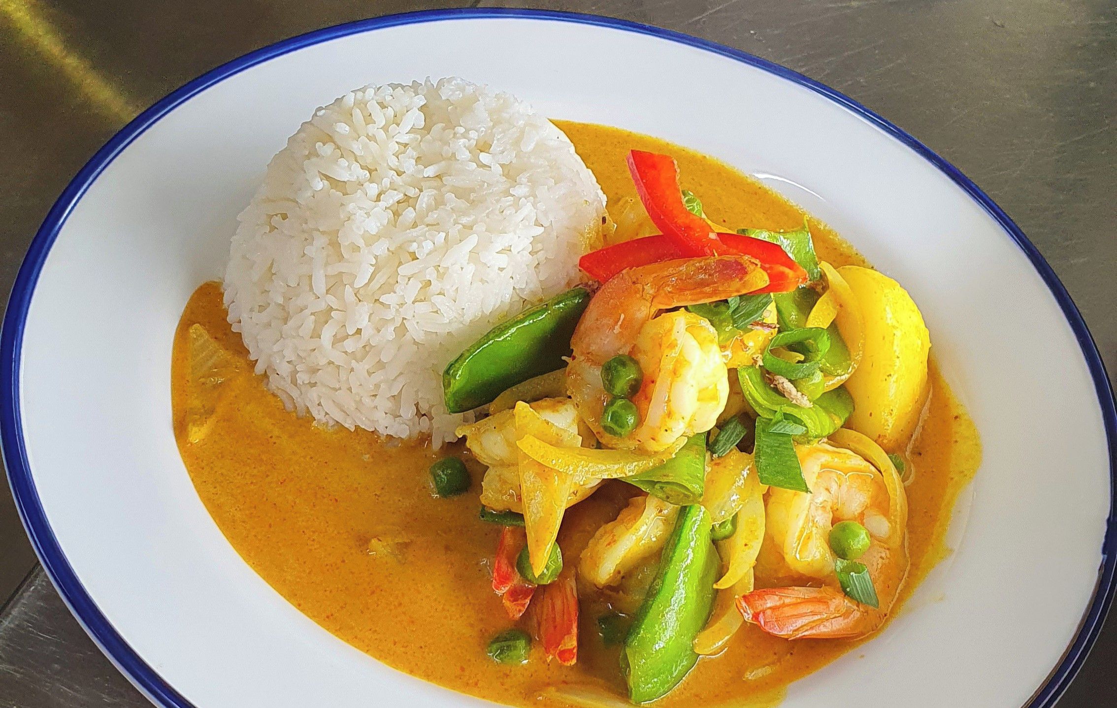 Un plato de langostinos al curry amarillo con arroz.