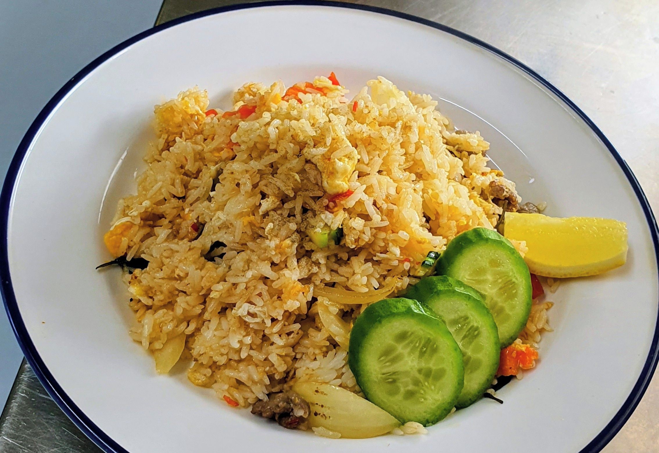 A plate of spicy fried rice with cucumber slices and a lemon wedge.