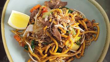 A plate of Hokkien Duck noodles with vegetables and a lemon wedge.
