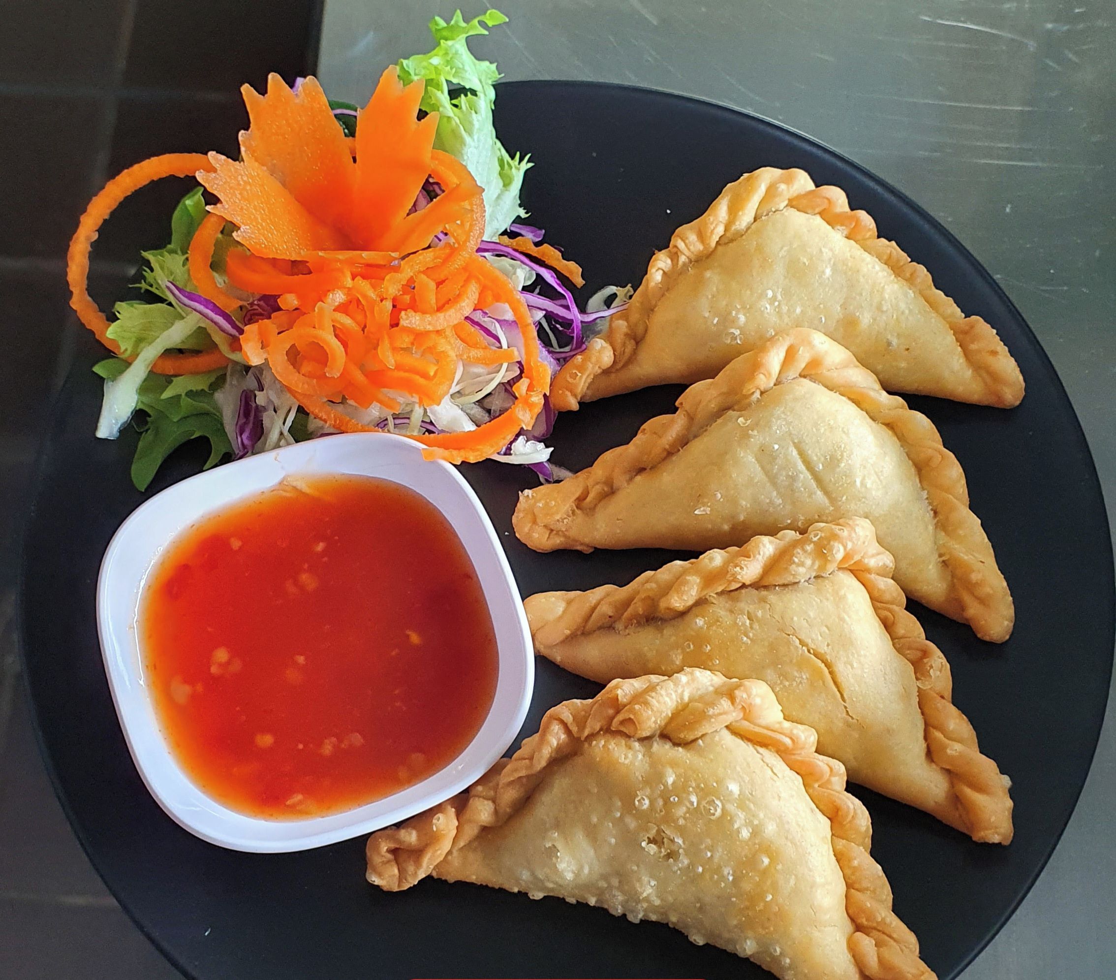 A plate of curry puffs with a side of carrot slaw and a bowl of sauce.