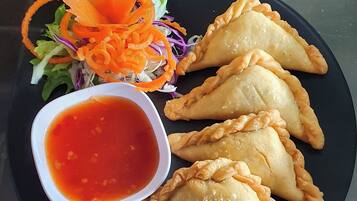 A plate of curry puffs with a side of carrot slaw and a bowl of sauce.