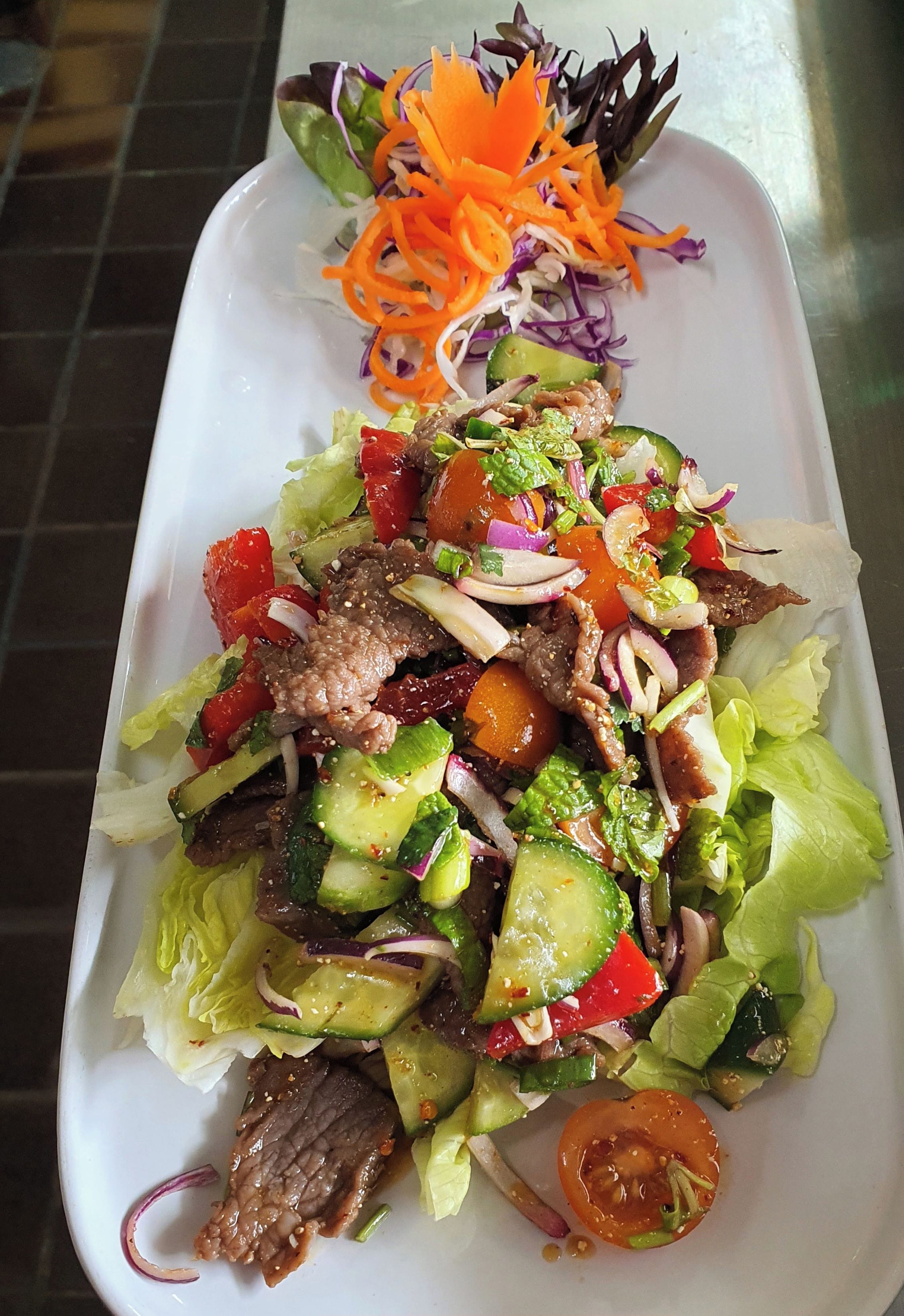 Ensalada tailandesa de carne con lechuga, pepino, tomate y zanahoria rallada.