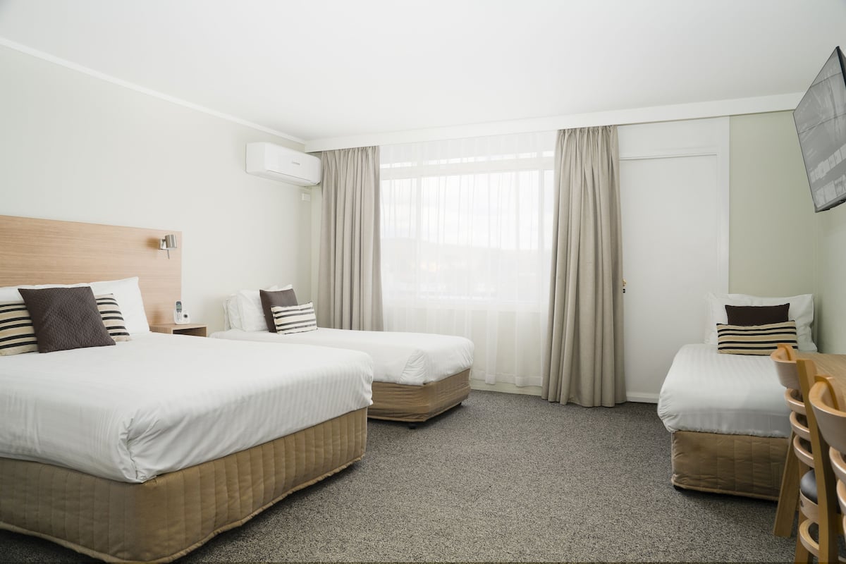 A hotel room with two beds, a desk, a chair, and a TV.