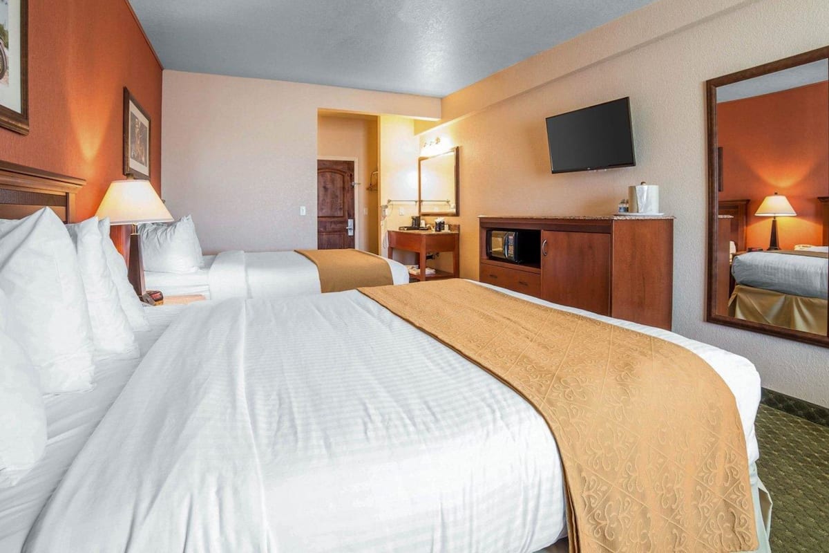A hotel room with two beds, a desk, a television, and a mirror.