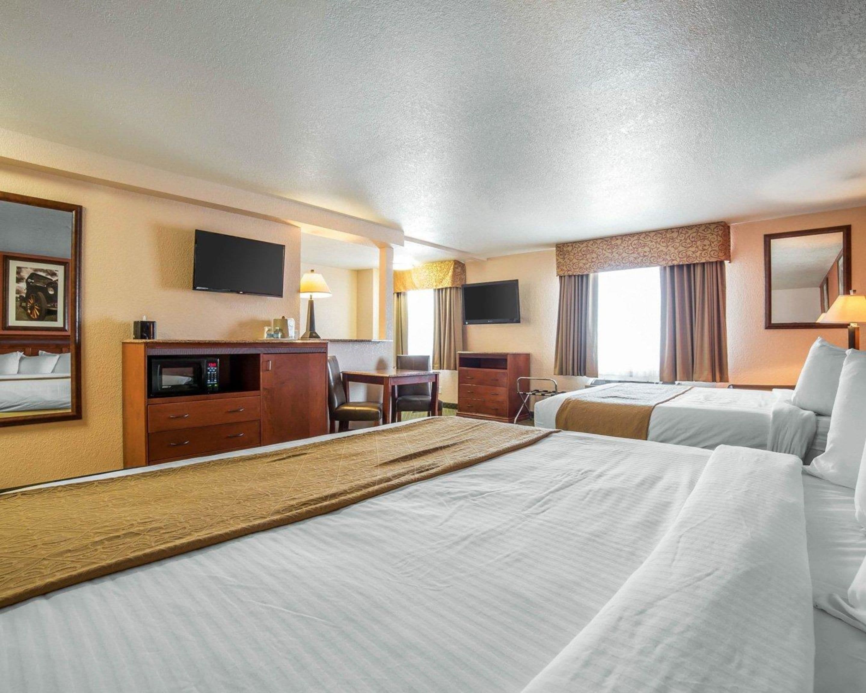 A hotel room with two beds, a desk, a chair, a television, and a flat-screen TV mounted on the wall.