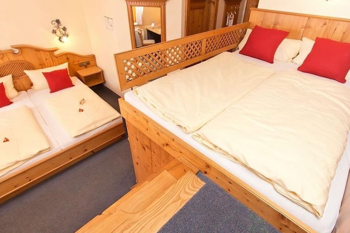Un lit double avec une tête de lit en bois, deux lits simples avec des oreillers rouges, un miroir et une armoire en bois.