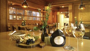 Ein Holzinterieur mit einem für eine Mahlzeit gedeckten Tisch, inklusive einer Weinflasche, Gläsern sowie einer Käse- und Obstplatte.