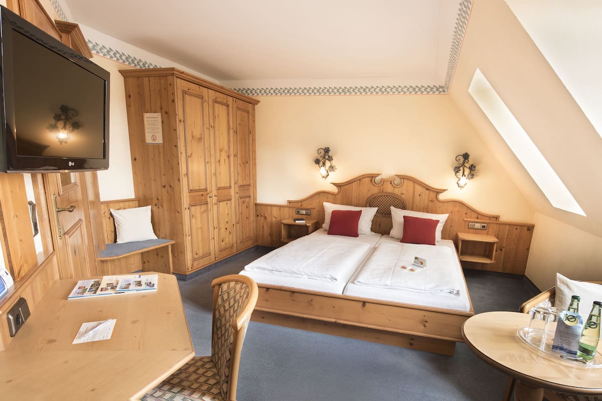 Une chambre d’hôtel avec un grand lit, des meubles en bois, une télévision et une petite table avec des bouteilles.