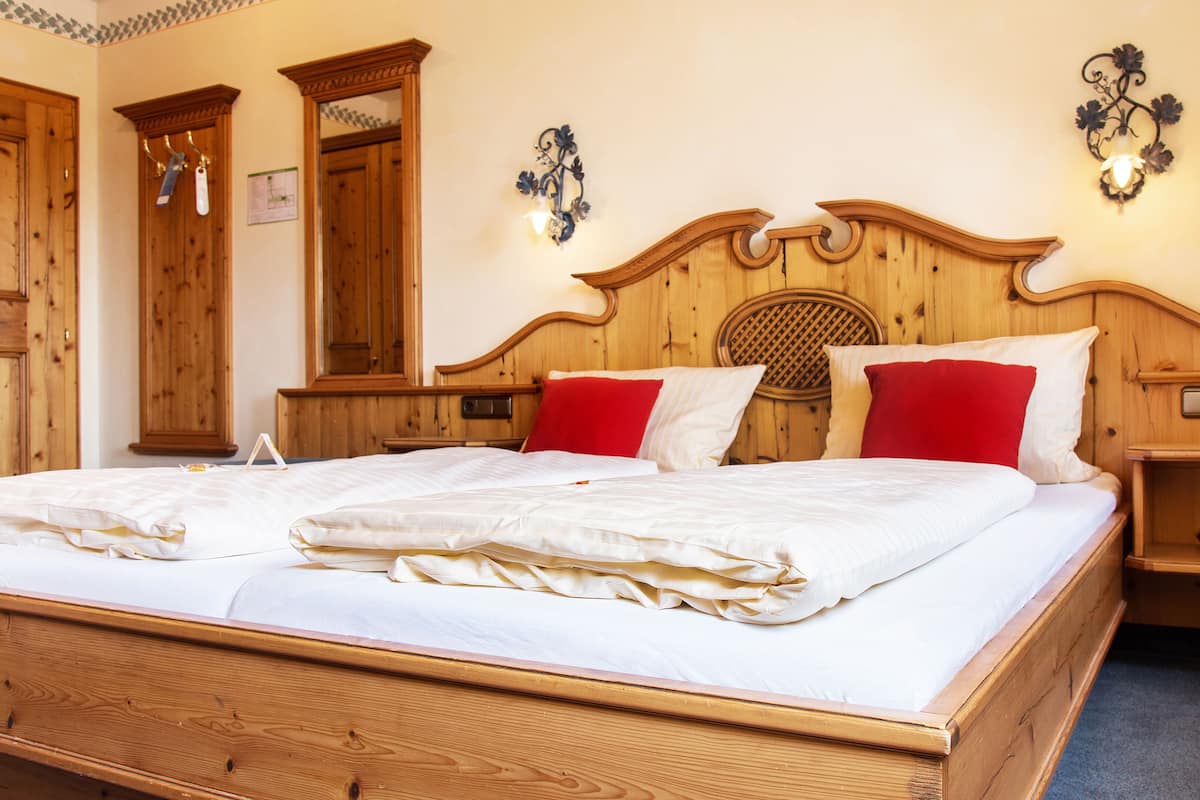 Un lit à baldaquin en bois, agrémenté de draps blancs et d’oreillers rouges, une table de chevet en bois et un luminaire fixé au mur.