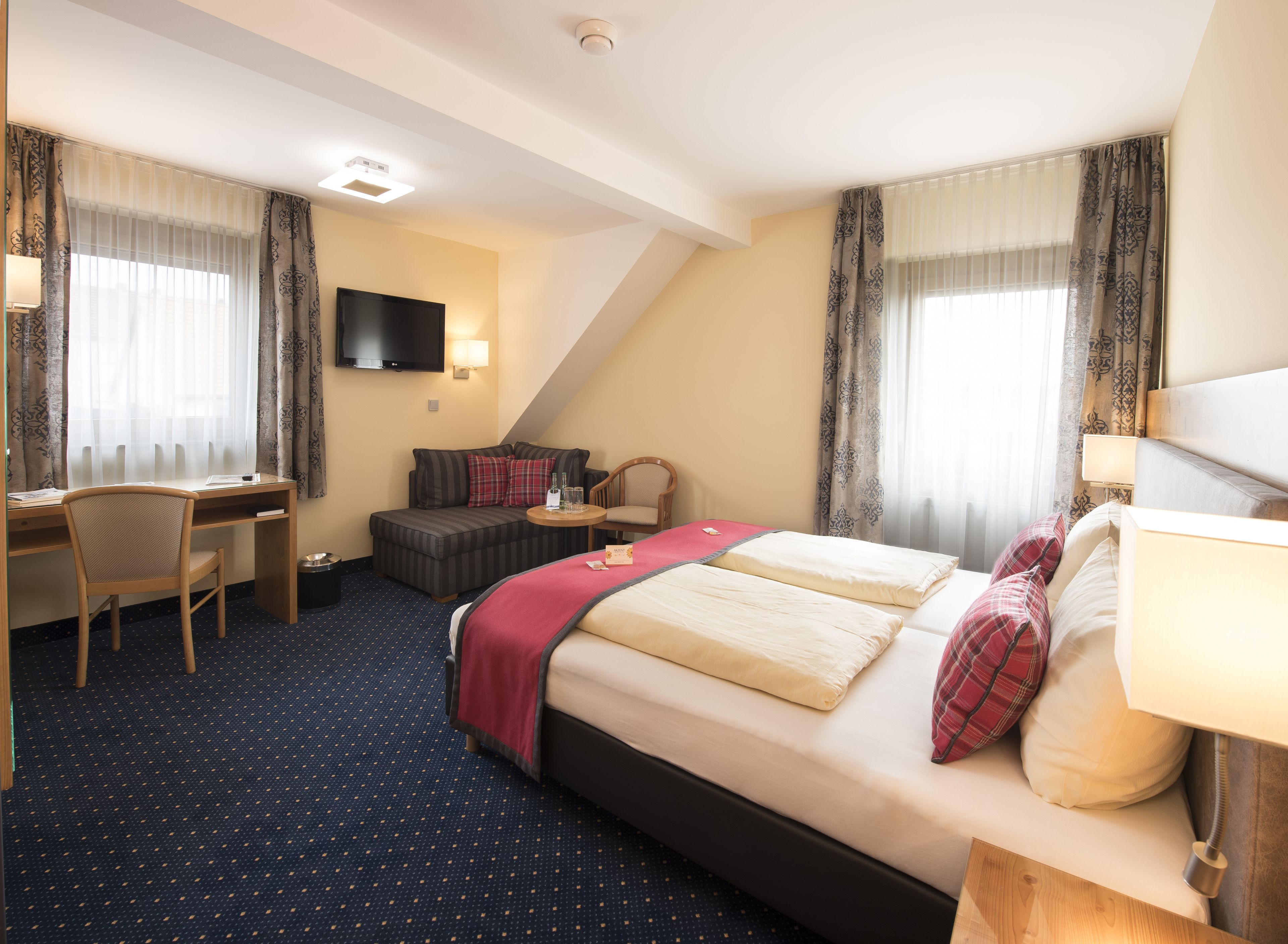 Une chambre d’hôtel avec un lit, un bureau, une chaise, une télévision et une petite table avec une lampe.